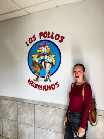 A woman stands in front of the sign at Los Pollos Hermanos on a self-guided Breaking Bad tour.