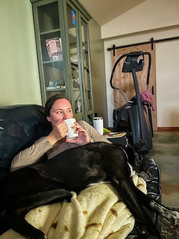 A woman sips on her coffee with a dog in her lap.
