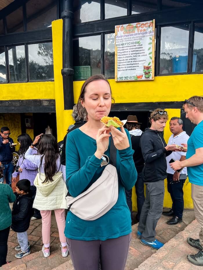 A woman eats a snack outside of a snack stand in Colombia.