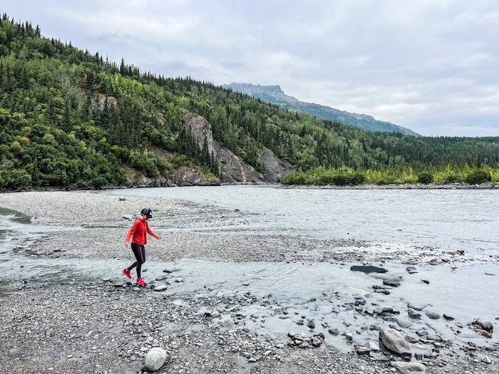 A woman hops near a river on a drive from Anchorage to Denali.