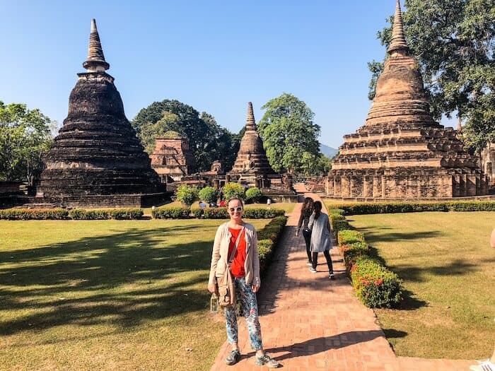 A woman visits Sukhothai and poses in front of an ancient temple.