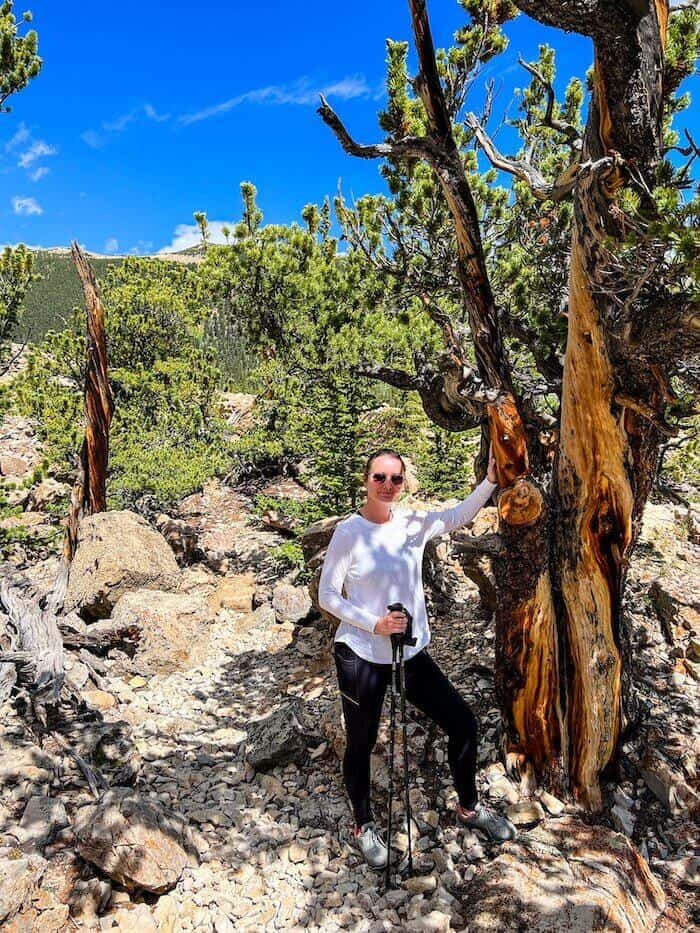 A woman poses against a tree on a hike.