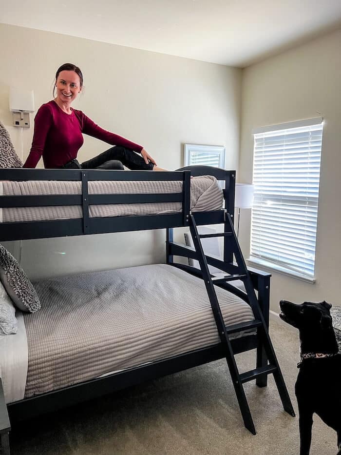 A woman poses on the top bunk with her dog looking at her from below.