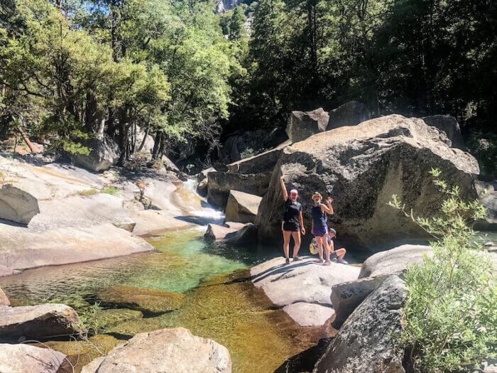 Two women stand waving on a rock at a national park.