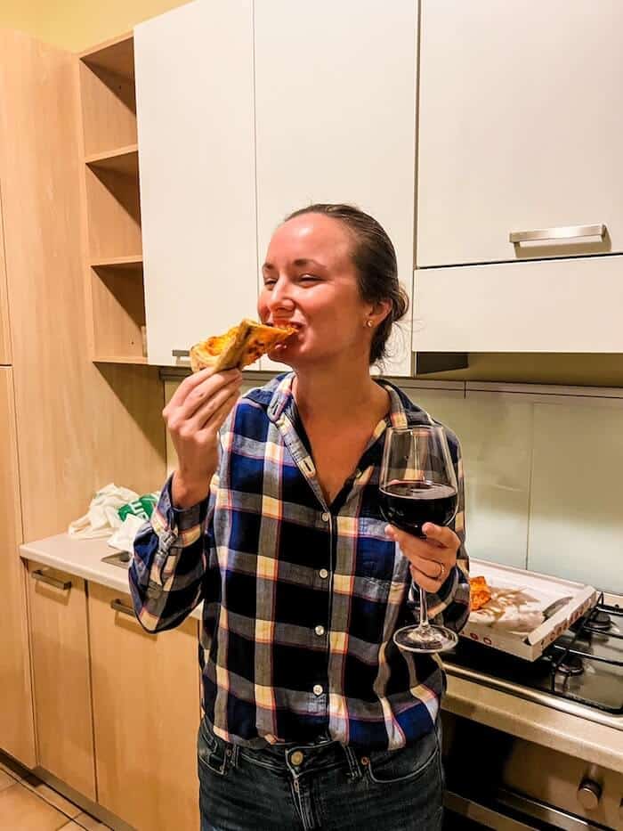 A woman eats pizza and drinks wine as a response to, "Is Bologna worth visiting?"