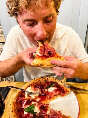 A man eats pizza as a response to, "Is Bologna worth visiting?"