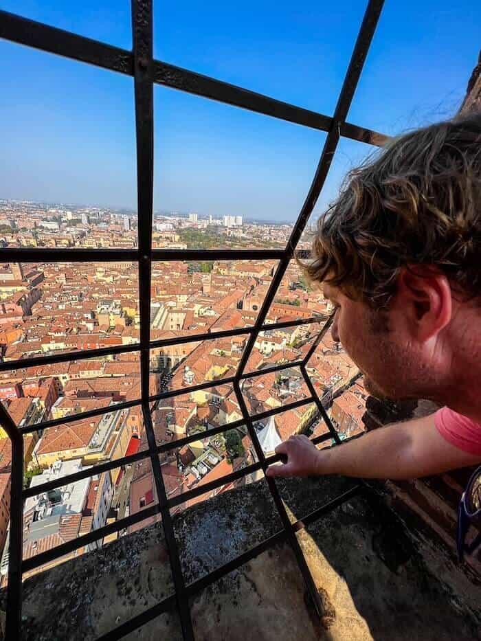 A man looks down at a view from a Bologna tower as a response to, "Is Bologna worth visiting?"
