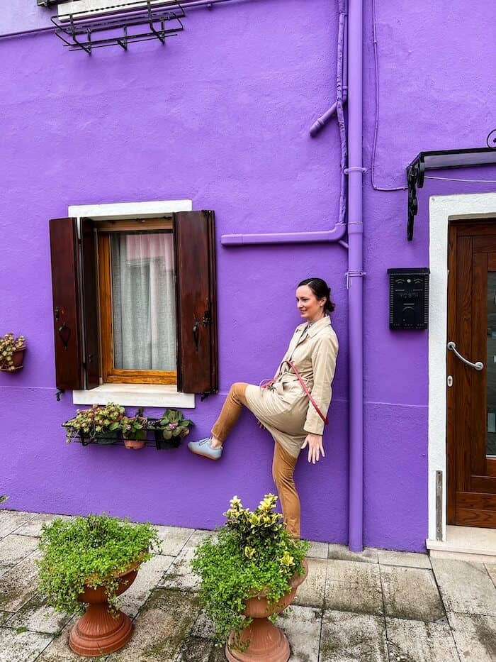 A woman poses against a purple home in Burano.