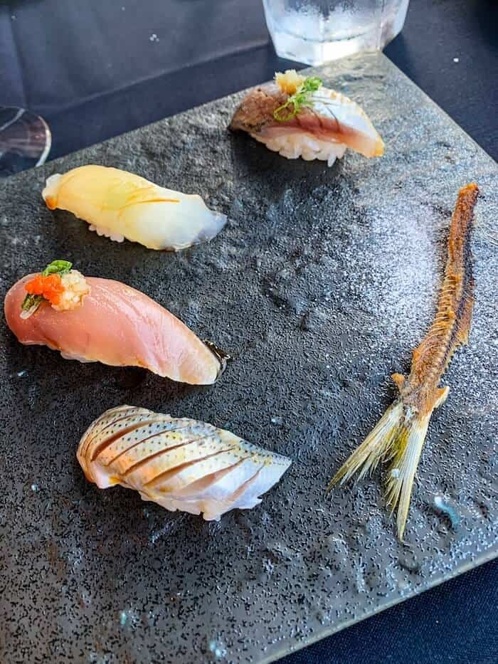 A plate of four pieces of sushi and a decoratively-placed fish bone at a sushi restaurant in San Diego, California.