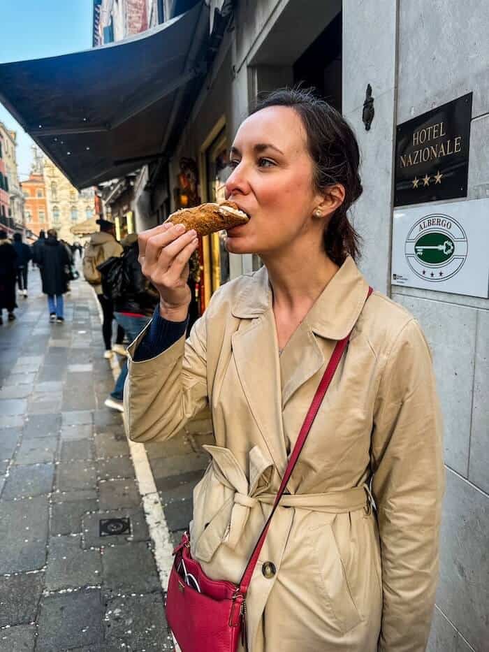 A woman eats a cannolo in Venice, Italy.