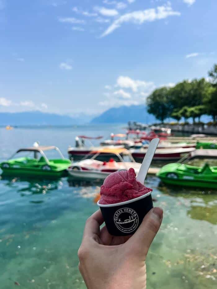 A woman holds up a cup of sorbet against Lake Geneva in Lausanne, Switzerland