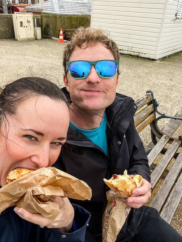 A couple poses with their sandwiches on a bench in France.