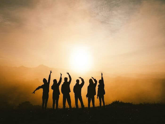 Friends with arms outstretched at a sunrise