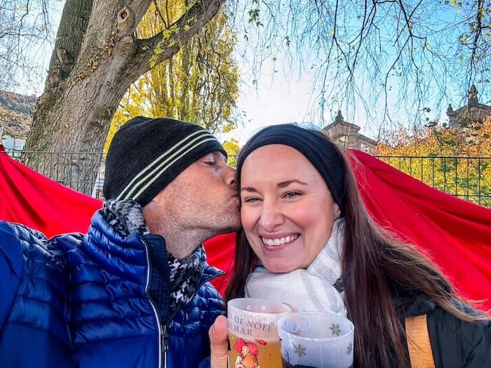 A man kisses his wife on the cheek at a Christmas market.