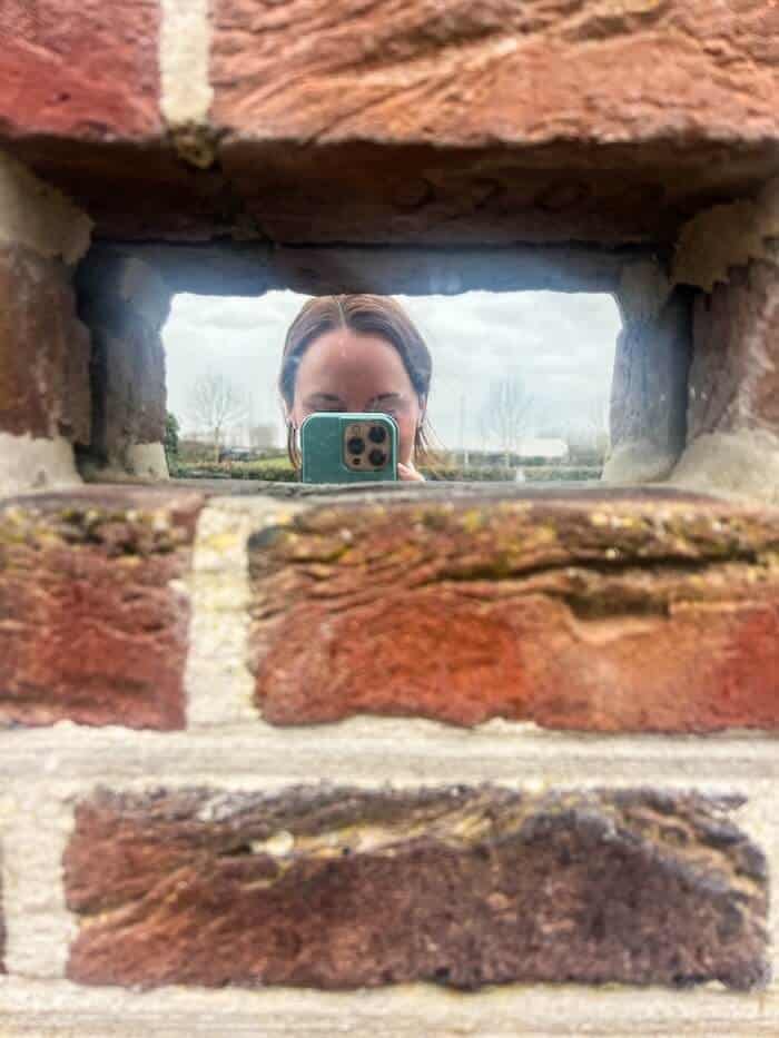A woman poses against a mirrored brick wall.