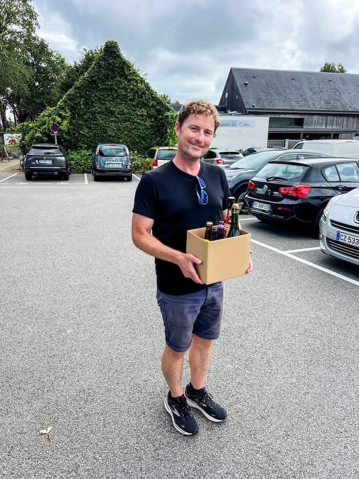 A man poses with a box of goodies at a cidery.