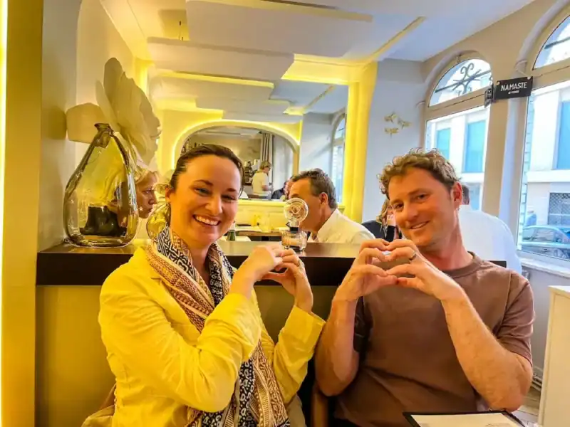 A couple poses with heart hands at a restaurant in Paris, France.