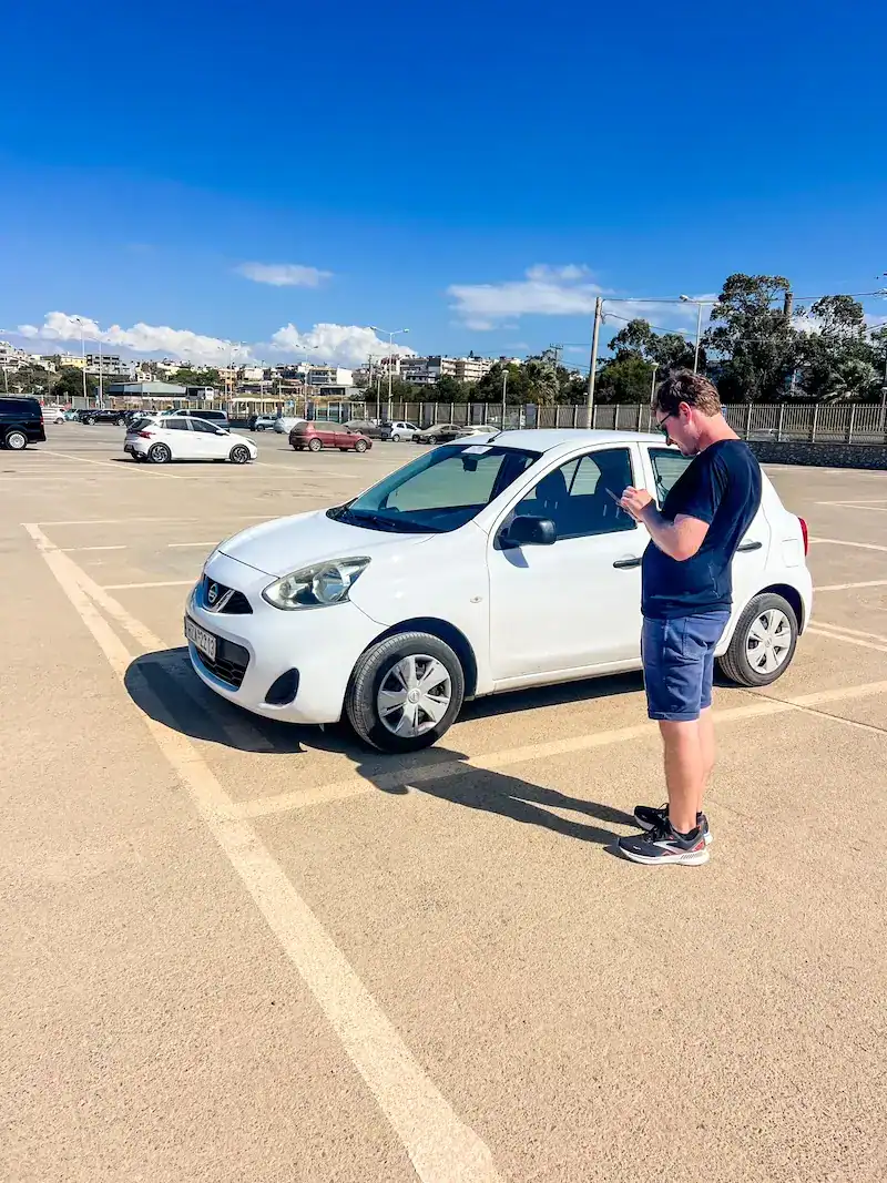A man stands near a rental car in Crete.