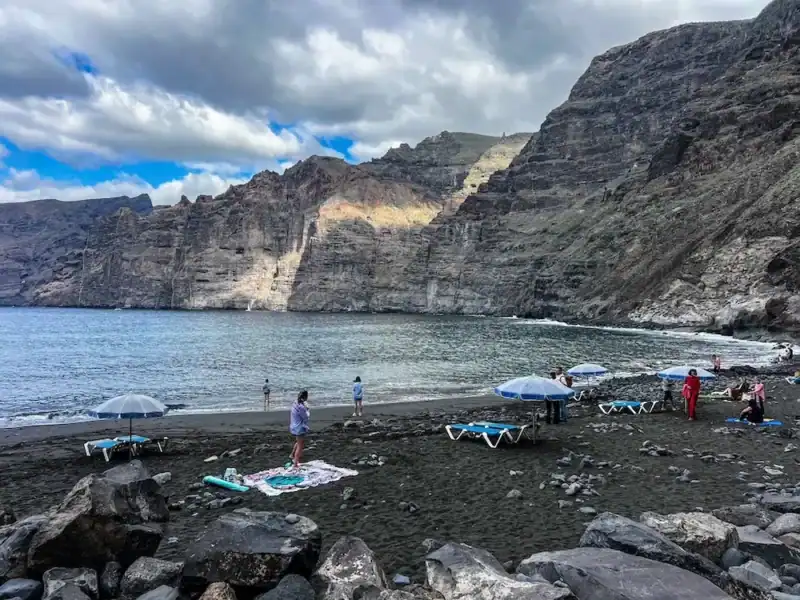 Tourists gather on a black sand beach in Tenerife.