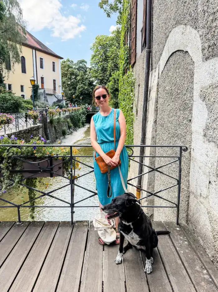 A woman poses with her dog near a pretty canal.