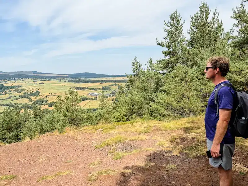 A man poses at the top of a hike while exploring volcanoes in France.