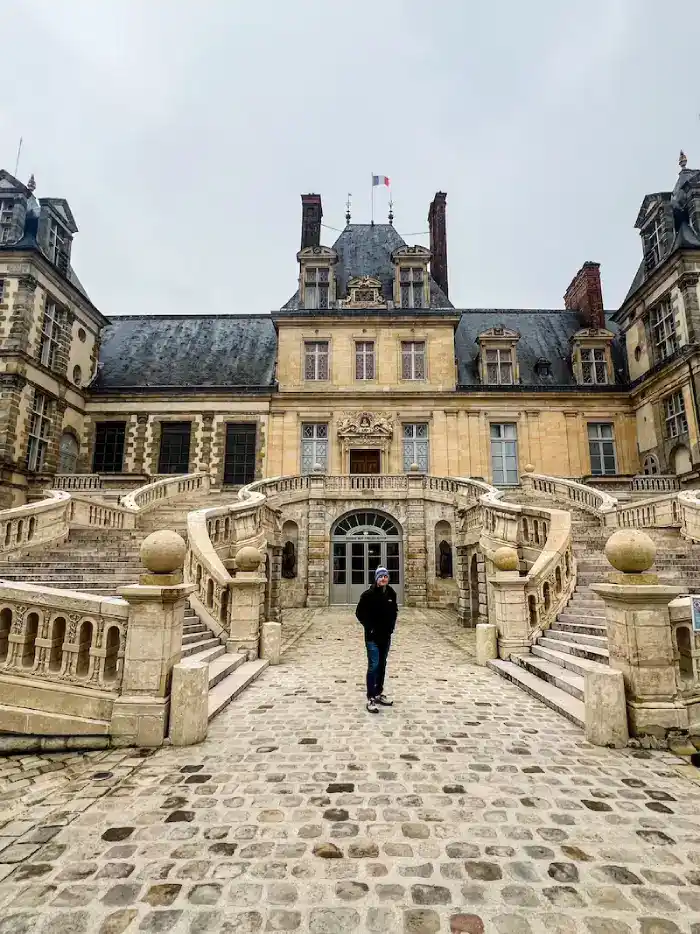A man stands in front of a castle in Fontainebleau on a day trip from Paris.